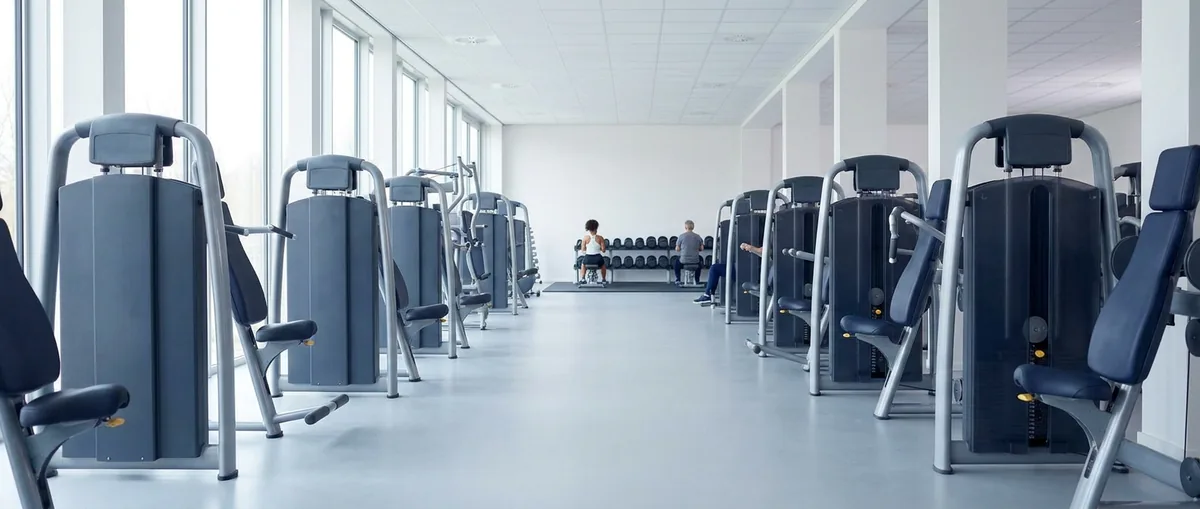 Een lange rij verschillende krachttoestellen in een lichte sportschool, met op de achtergrond een paar mensen die trainen: de dertig toestellen die je op de vloer tegenkomt